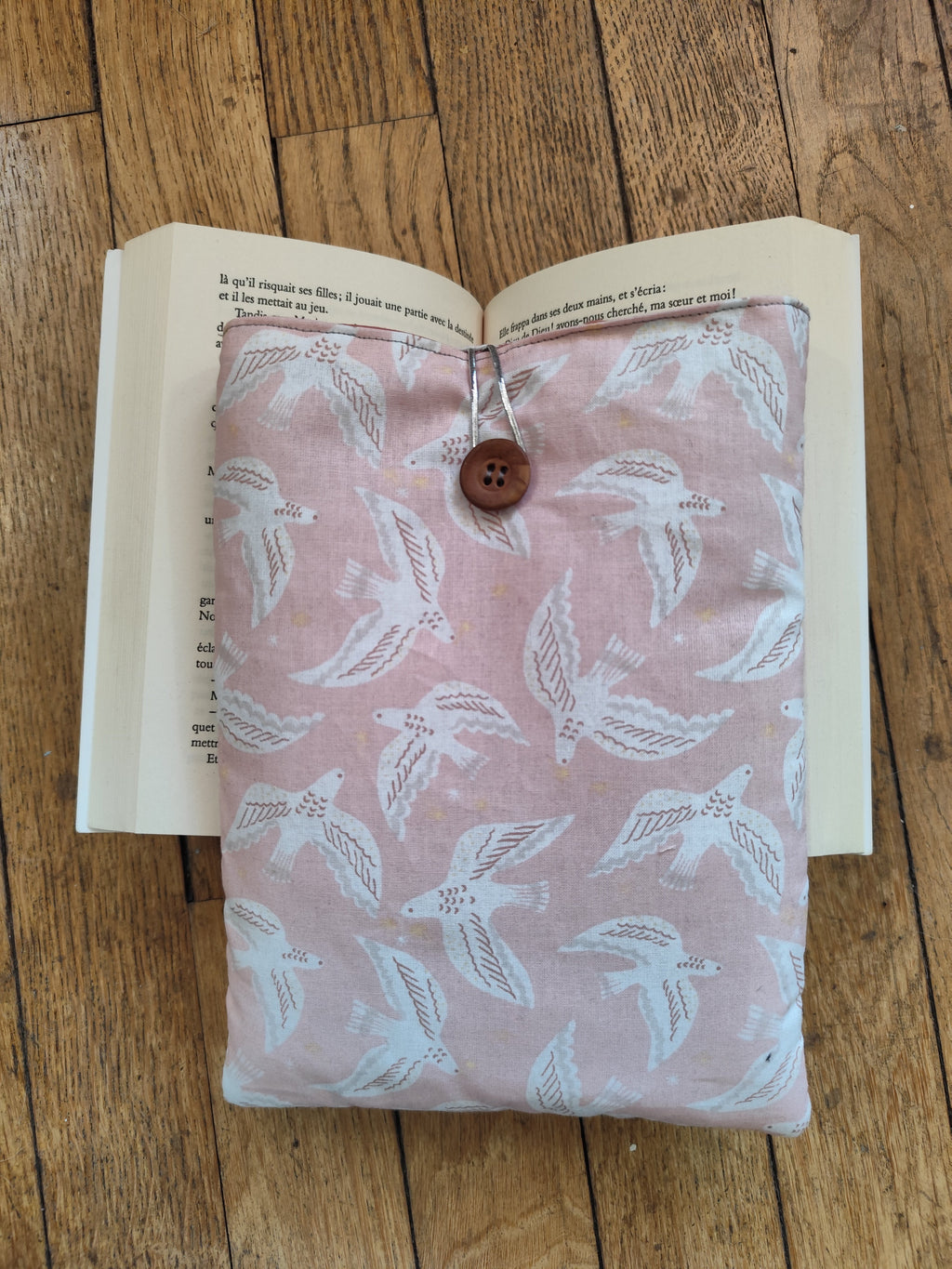 pochette Mouettes roses sur livre ouvert :
Housse de livre artisanale en coton imprimé mouettes blanches sur fond rose poudré, posée sur un livre ouvert, cousue à la main en région parisienne
