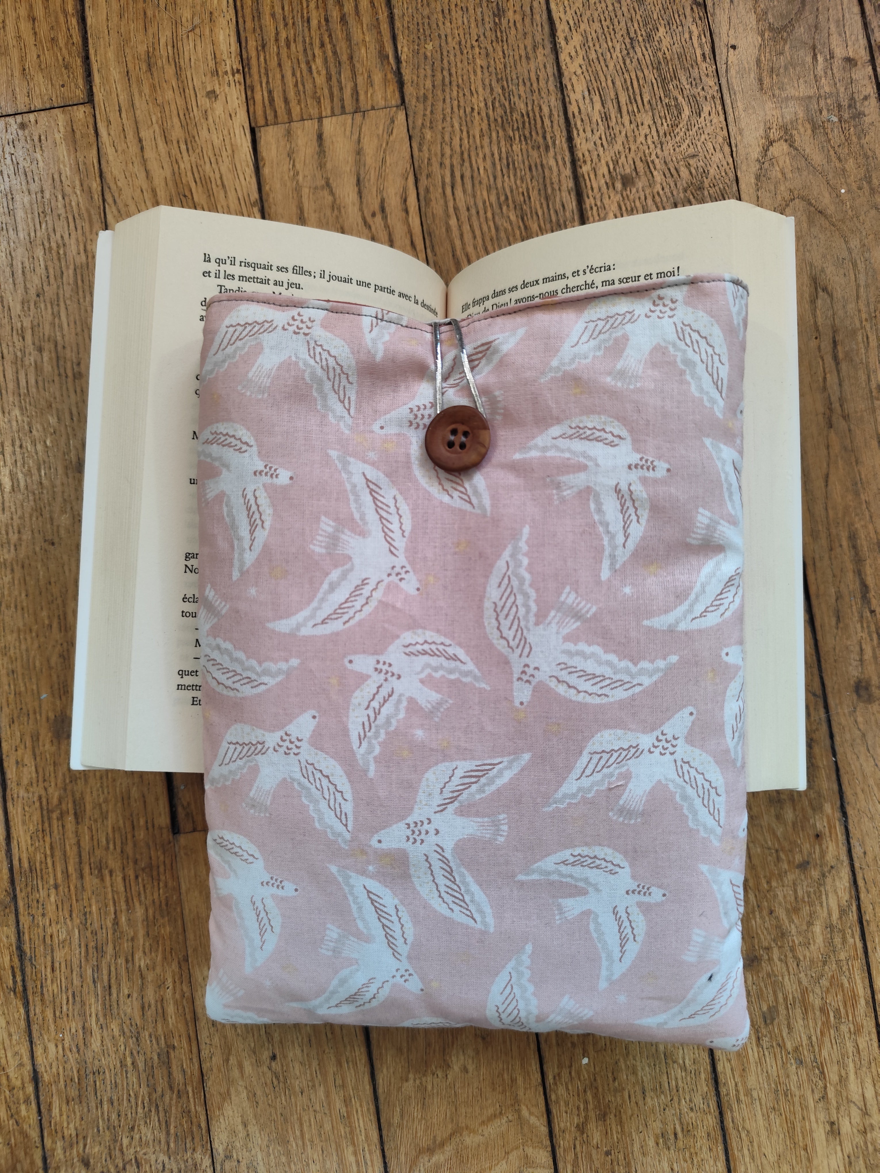 pochette Mouettes roses sur livre ouvert :
Housse de livre artisanale en coton imprimé mouettes blanches sur fond rose poudré, posée sur un livre ouvert, cousue à la main en région parisienne
